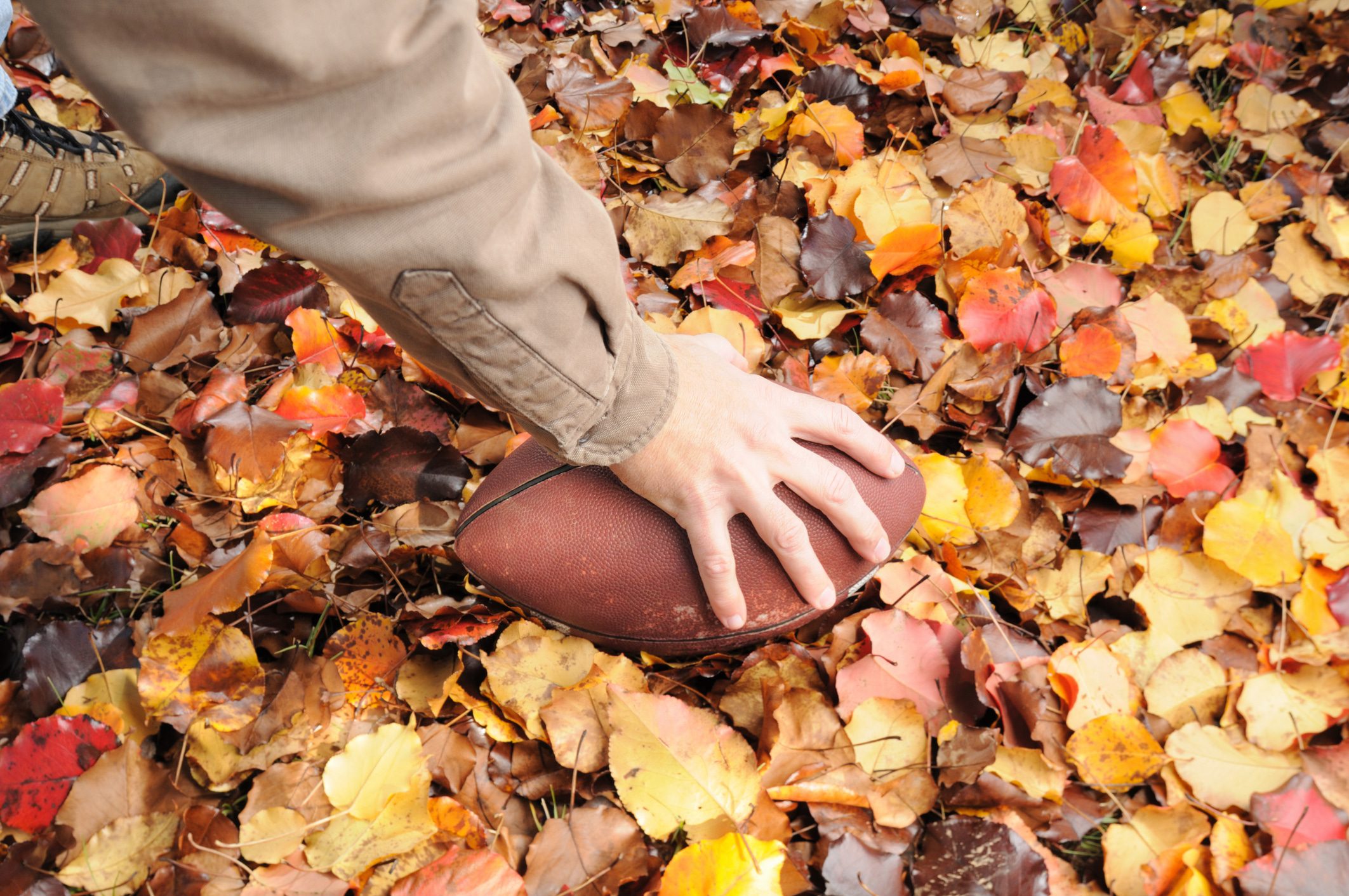 Hand about to throw football laying in pile of autumn leaves