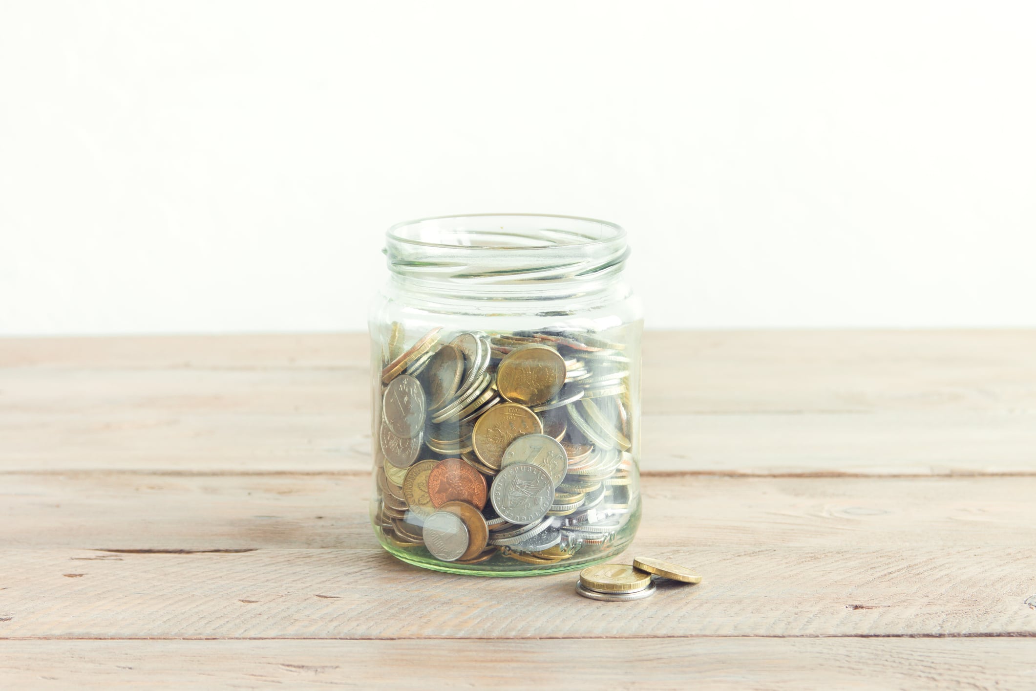 Coins in glass jar. Money savings concept. Jar with assorted coins on wooden table, copy space.