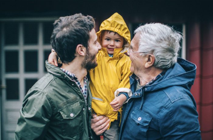 Father, son and grandson wearing rain jackets, smile at each other